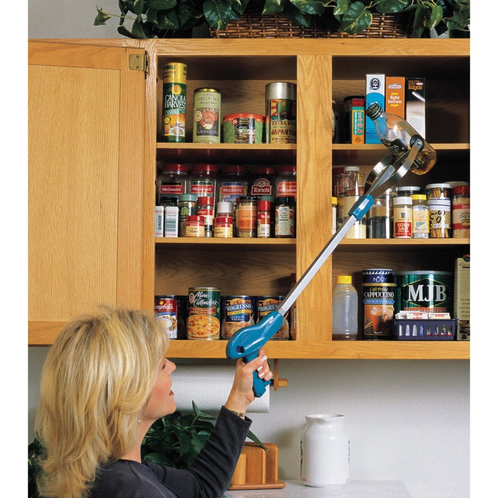 A blonde haired woman is using the ez grabber to get some olive oil off the top shelf in her cupboard